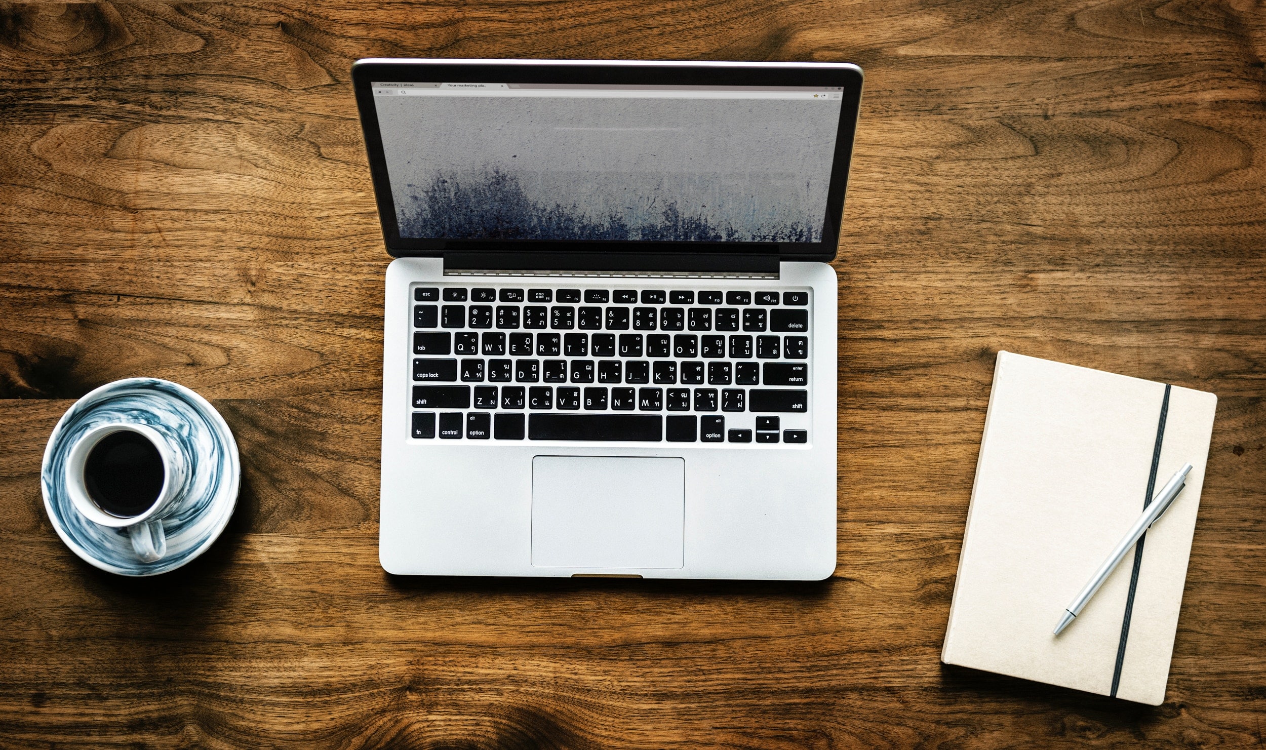 coffee mug (left), laptop (center), notebook with pen (right)