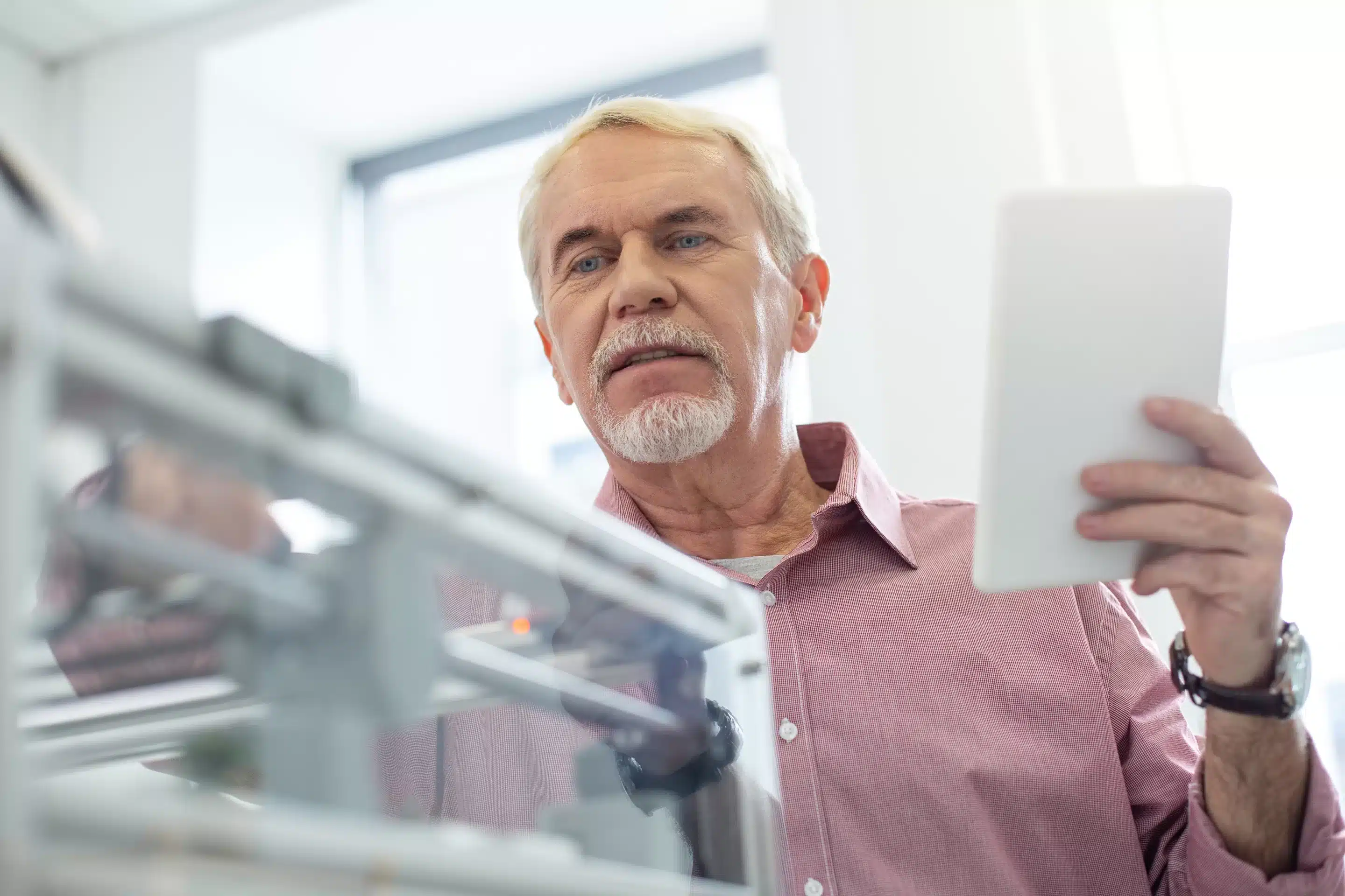 Important parameters. White-haired senior man setting up 3D printer with the help of tablet