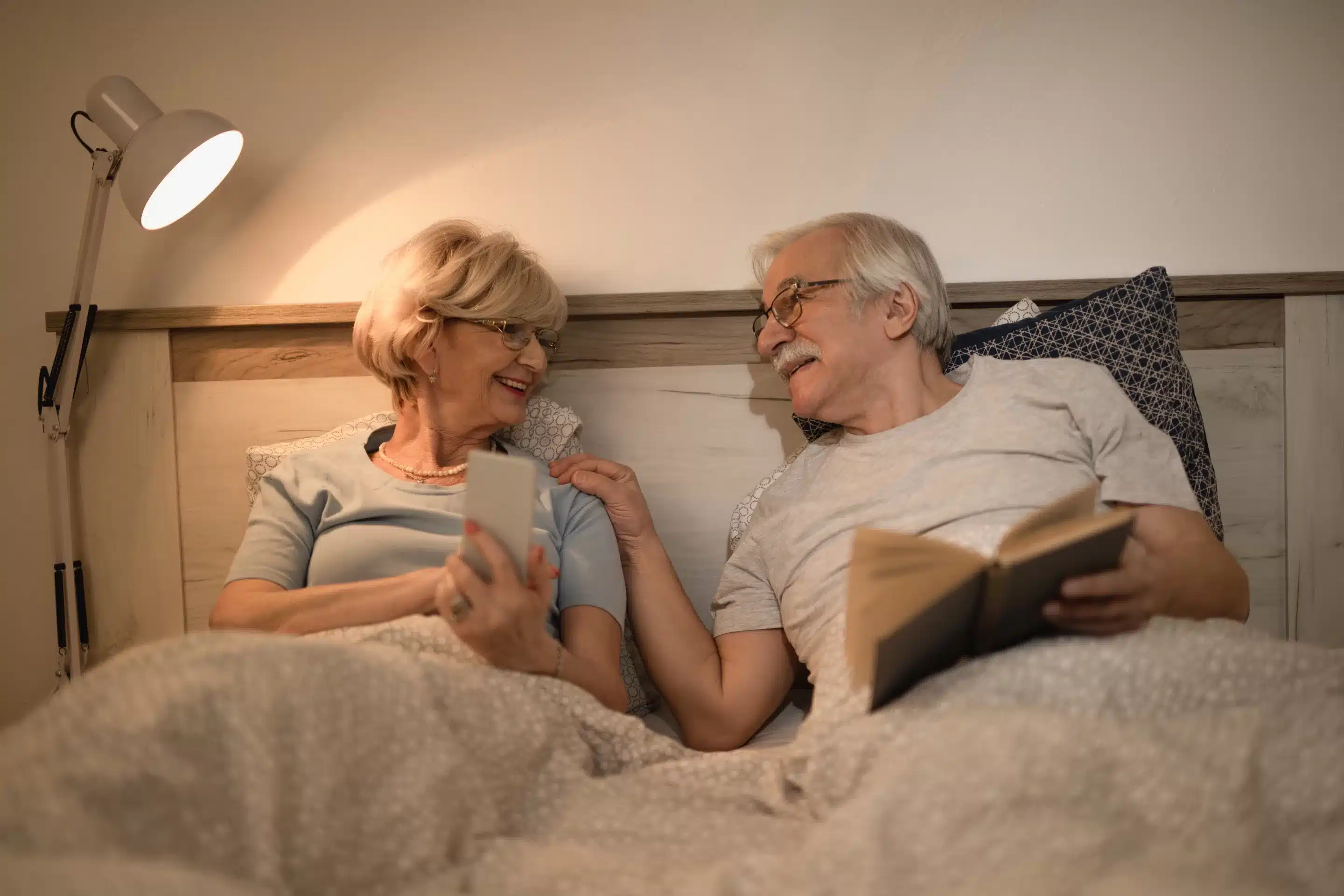 Happy senior couple resting in bedroom in the evening talking to each other.