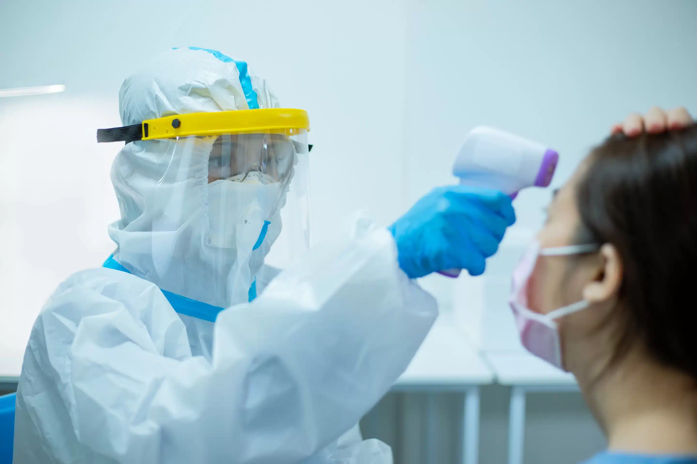 a person in hazmat suit measuring a woman's forehead