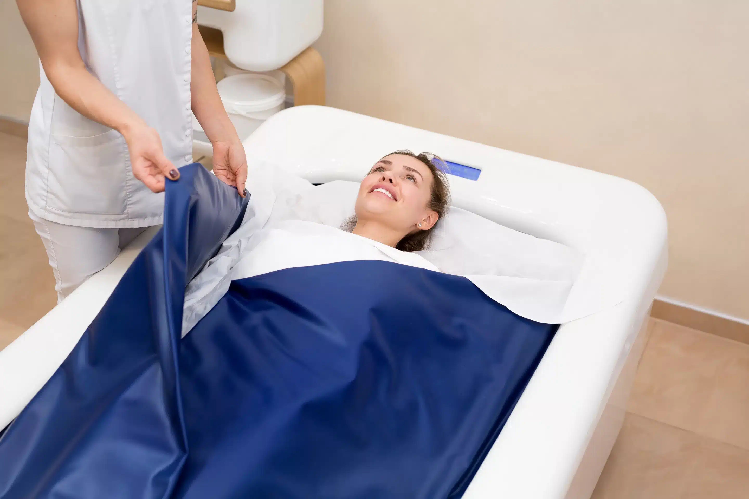 Cosmetologist covers the girl with a special blanket in the hydromassage bath.