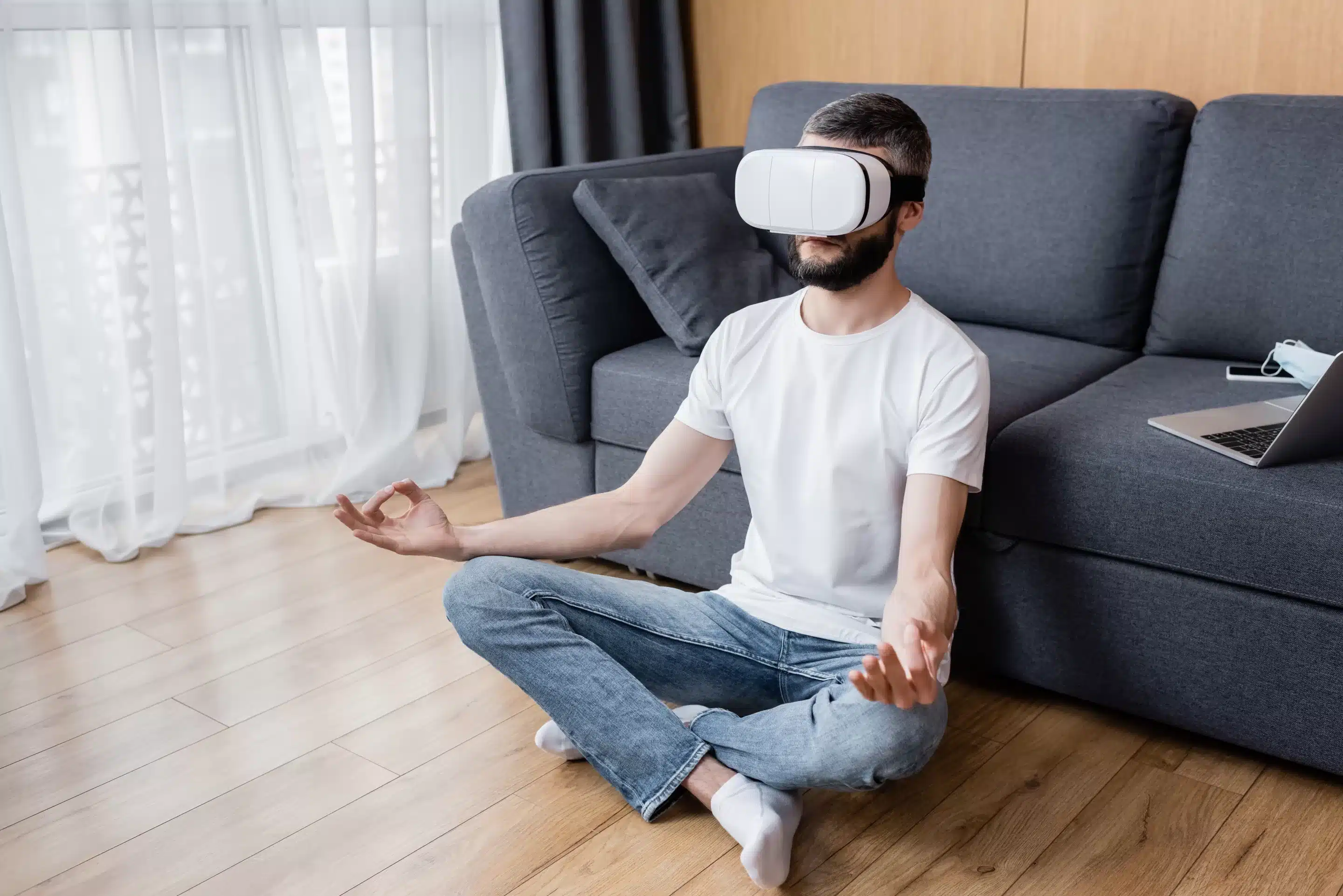 Man in vr headset meditating in lotus pose on floor in living room