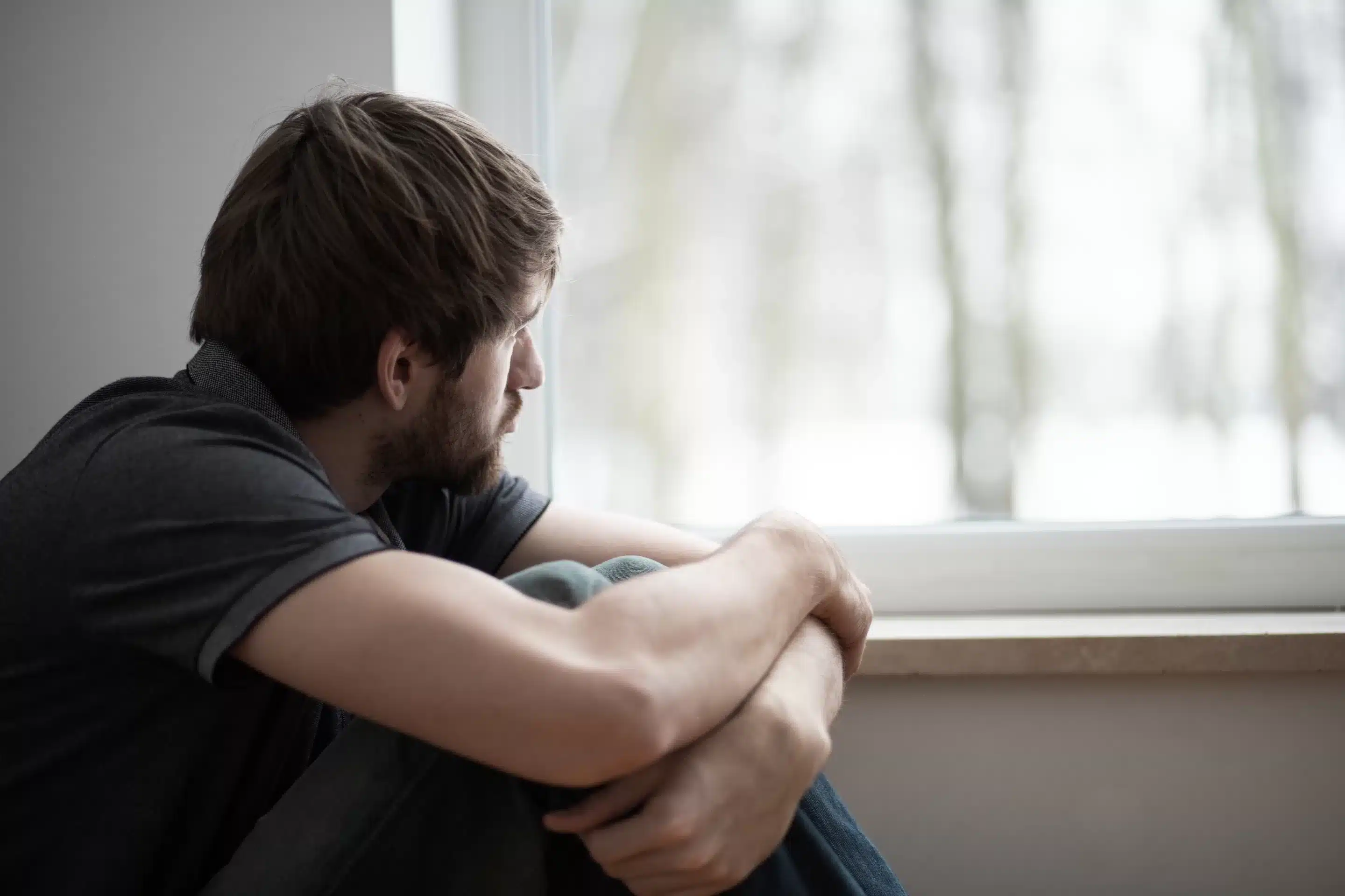 Sad young man sitting on the floor looking through the window