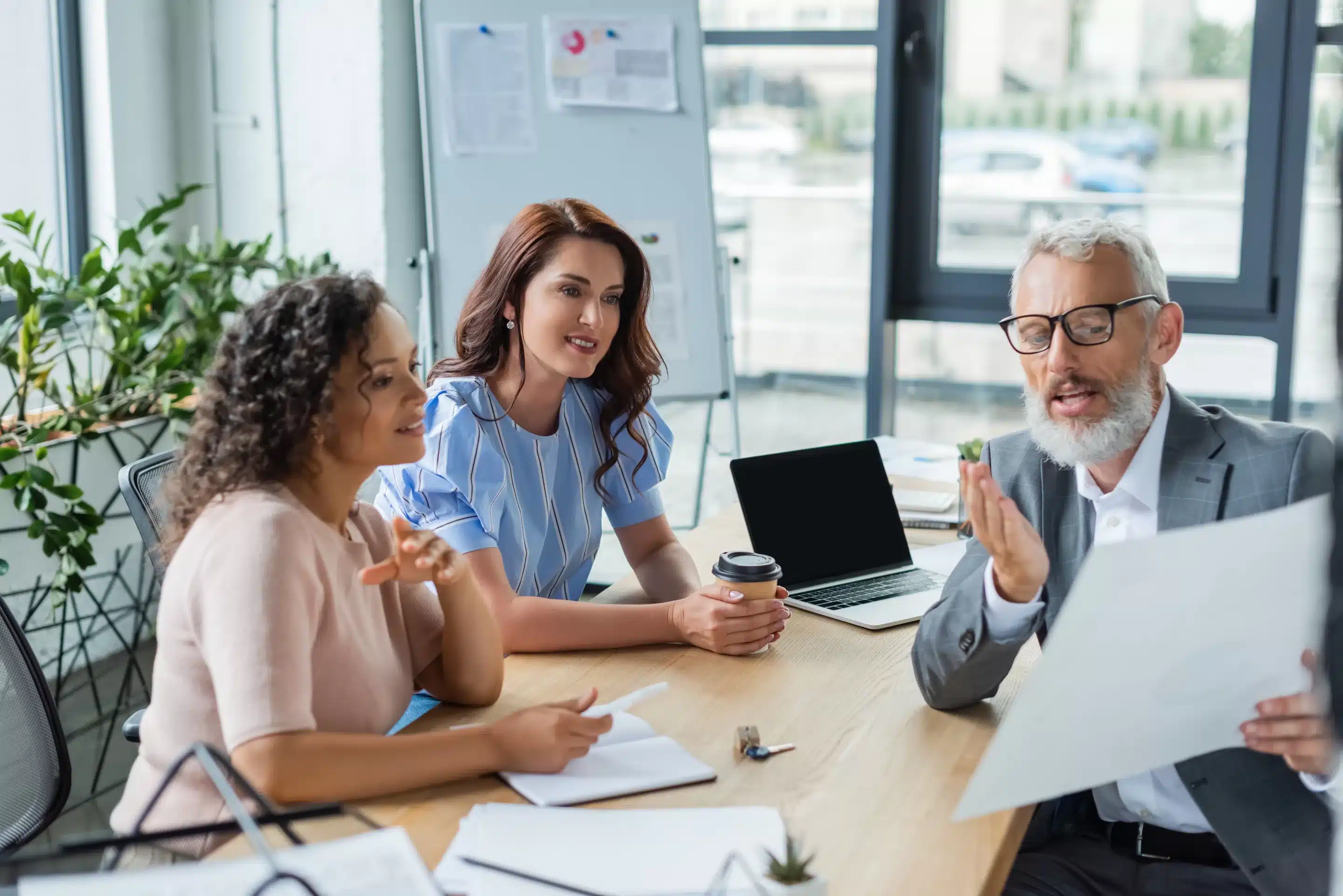 middle aged realtor showing document to multiethnic lesbian couple in real estate agency