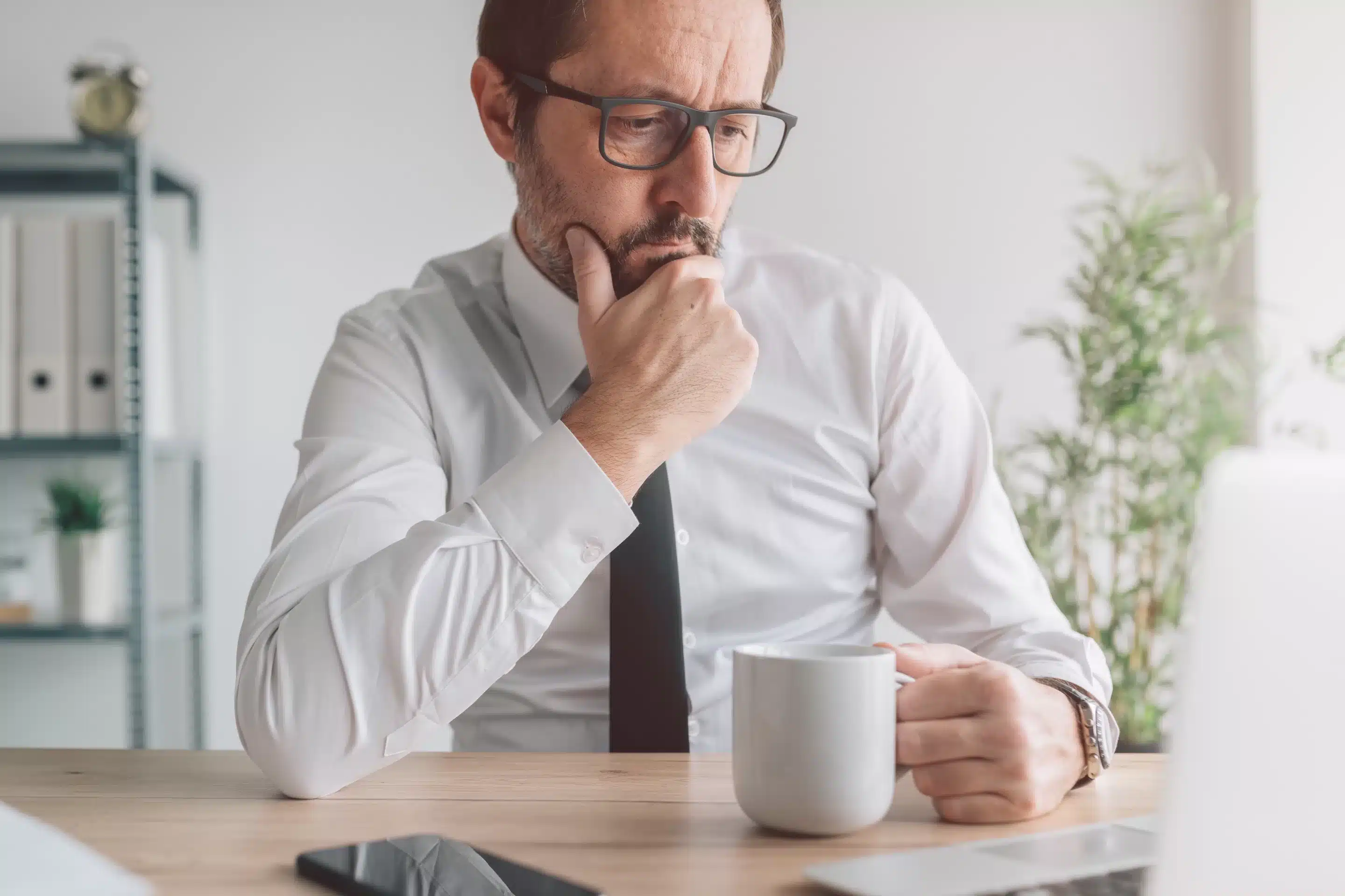 Portrait of perturbed businessman with cup of coffee in the office looking at laptop computer screen and thinking, selective focus