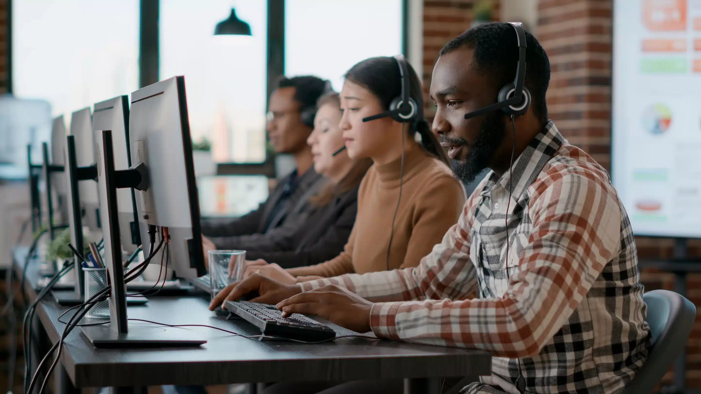 Three people sitting in front of computer screens with an enormous white wall behind them, they are anonymous