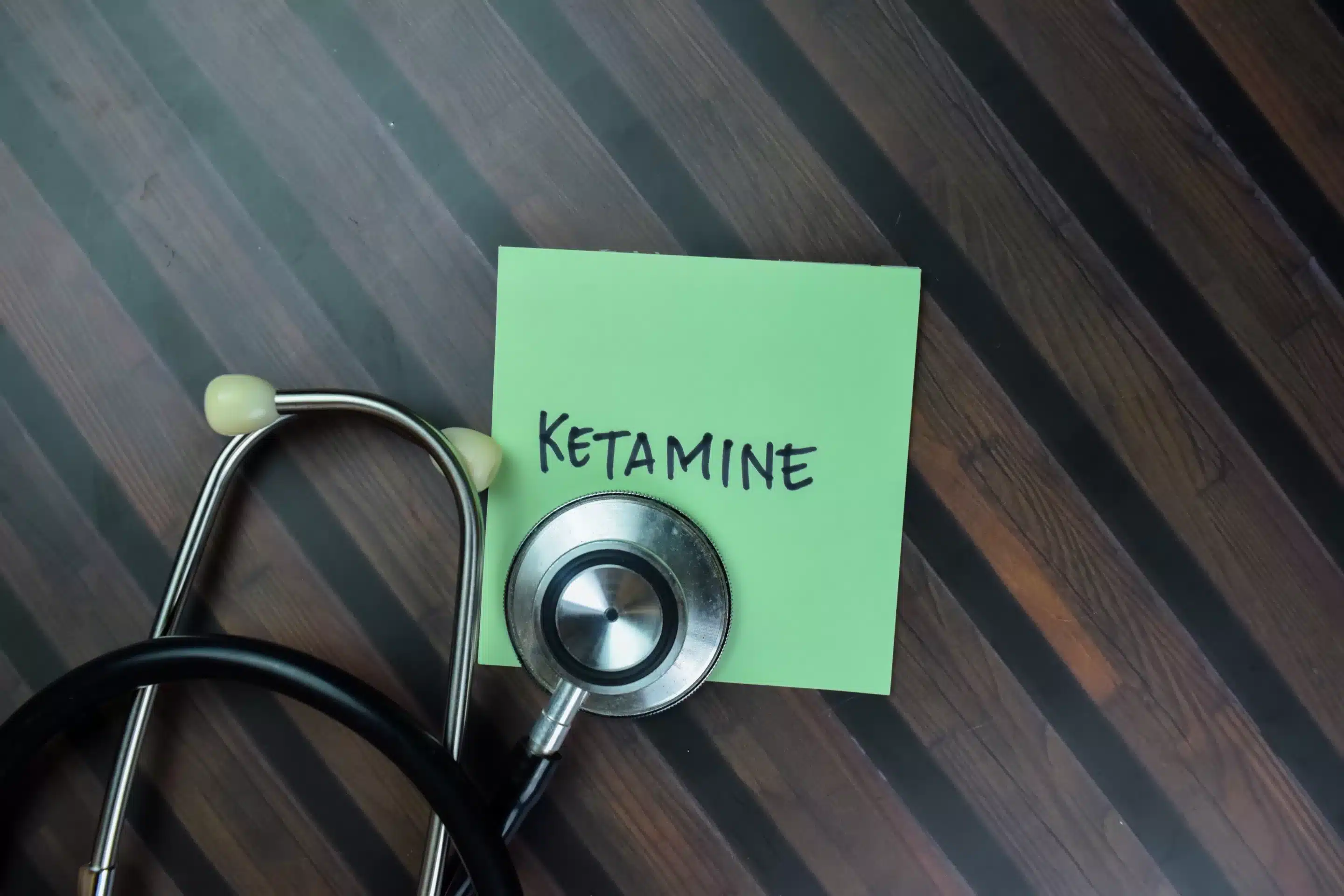 Concept of Ketamine write on sticky with stethoscope notes isolated on Wooden Table.