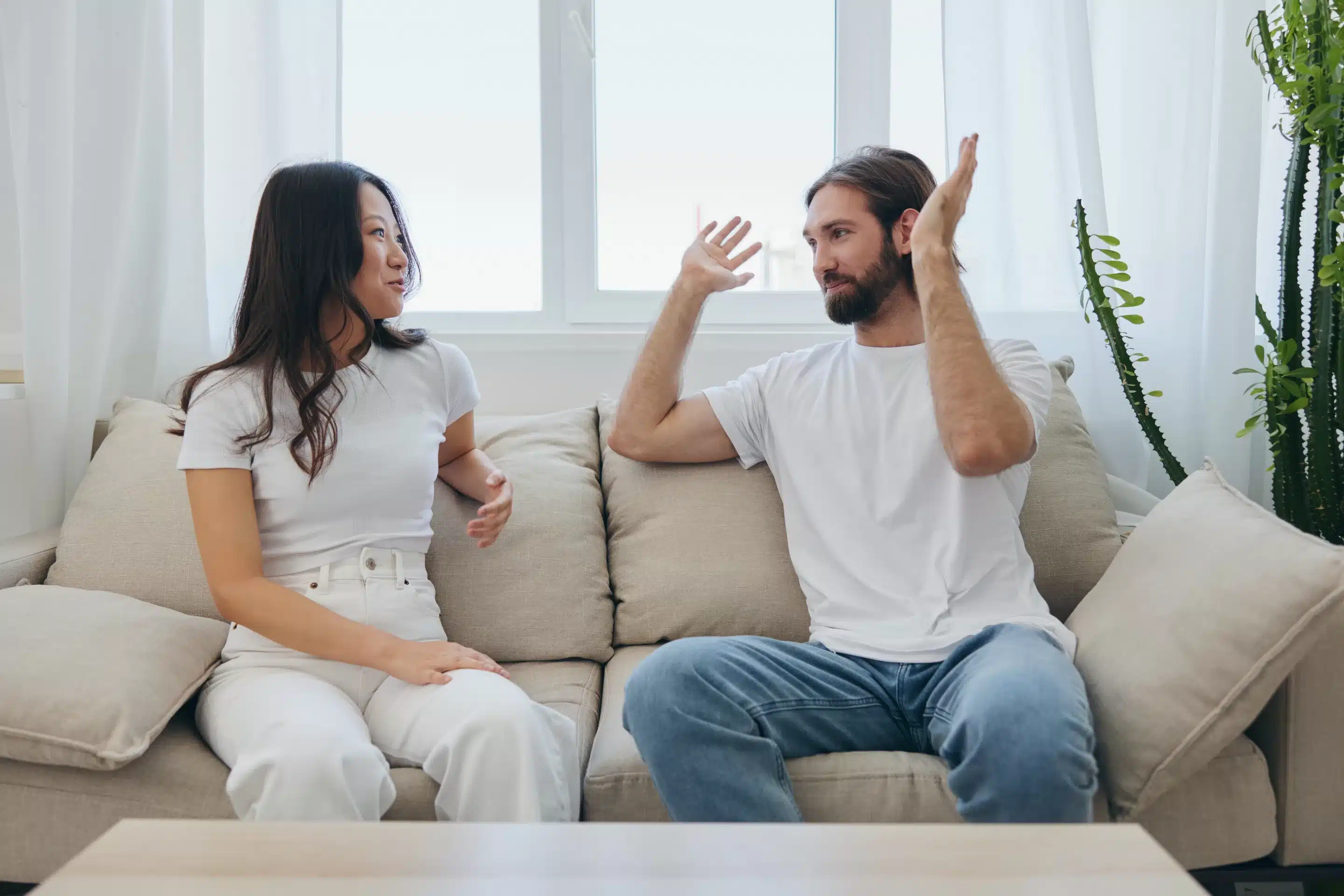 A man and a woman sitting at home on the couch in white stylish t-shirts