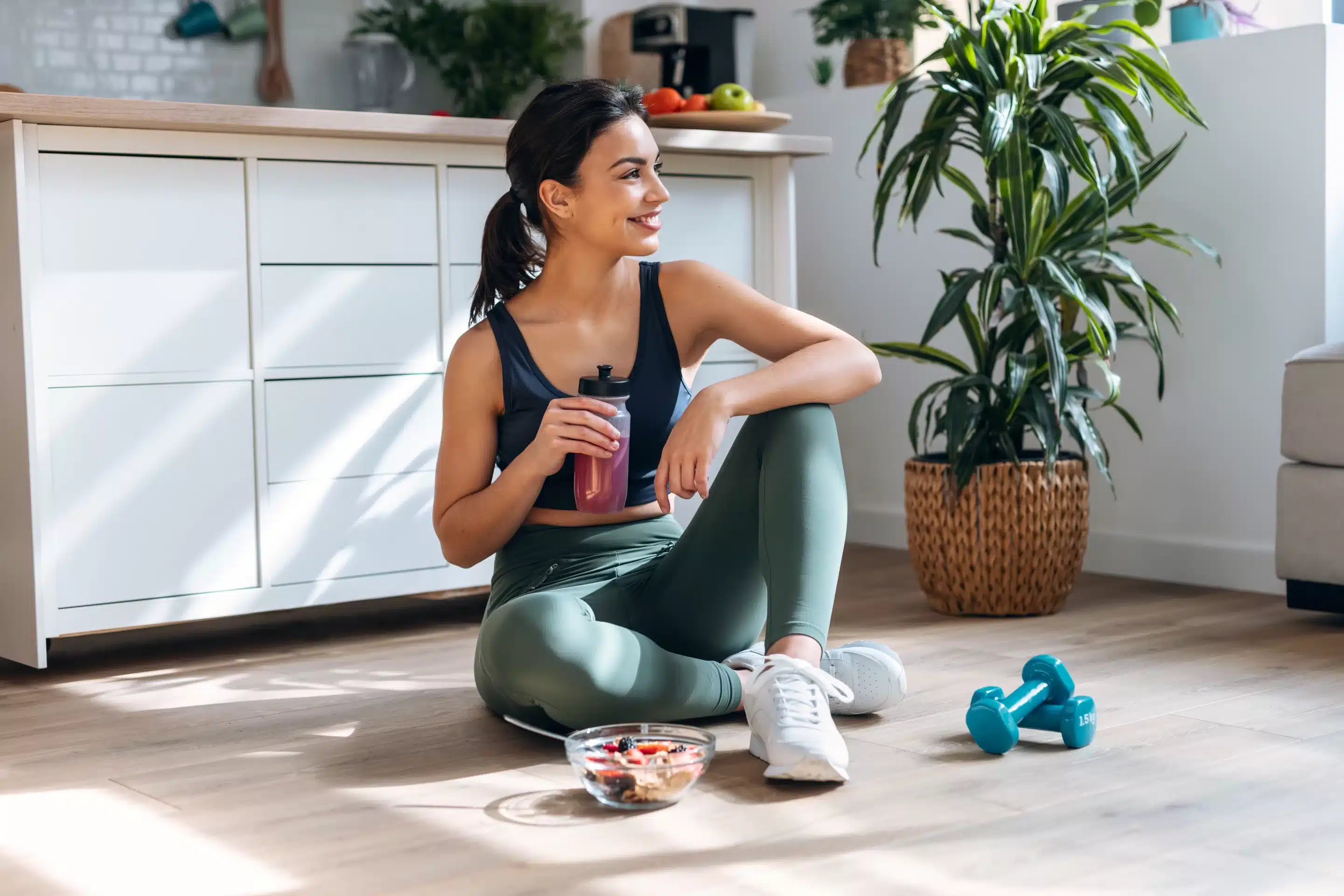 Shot of athletic woman drinking healthy protein shake while sitting on floor