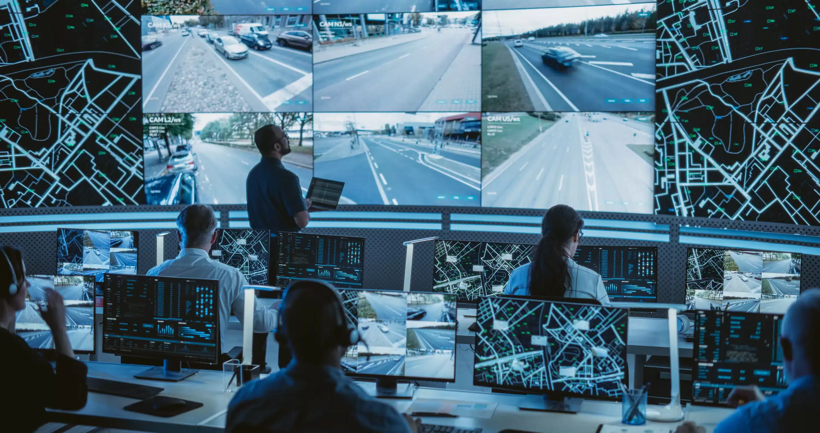 Male Software Engineer Working on Laptop Next to a Big Screen in a Modern Monitoring Office