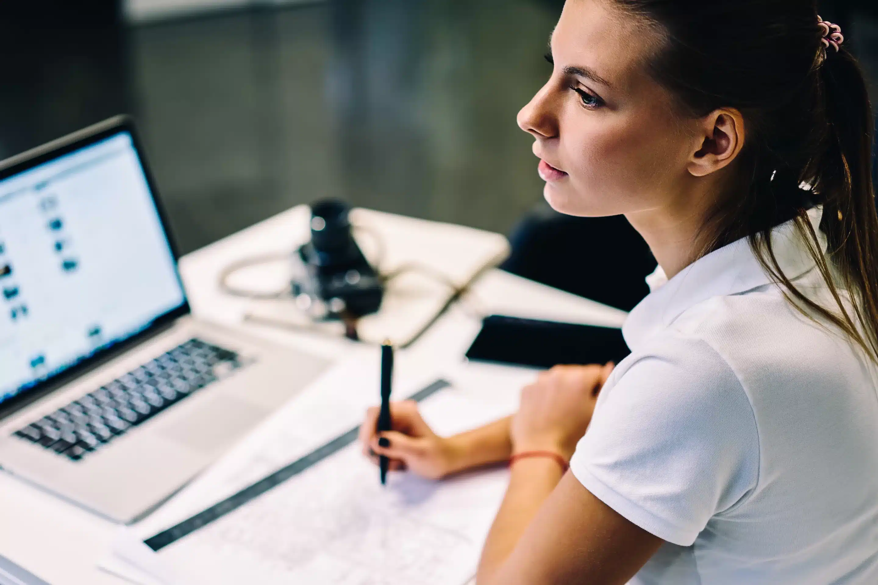 a woman sitting at a desk with a laptop and a pen