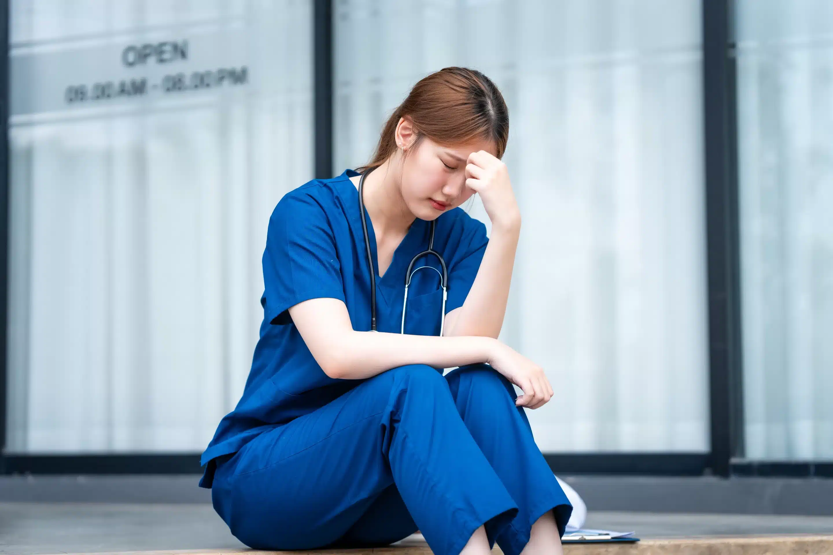 Physician Burnout a woman in blue scrubs sitting on a step