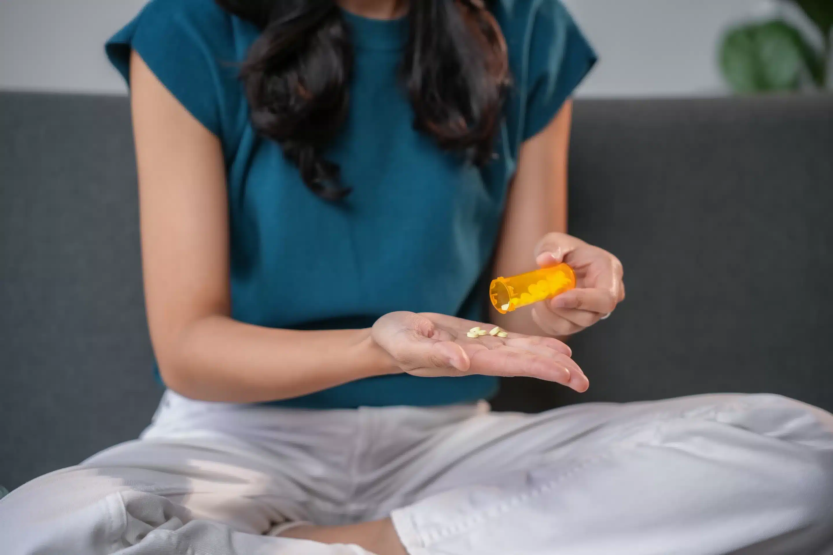 Young woman is pouring pills from a prescription bottle into her hand