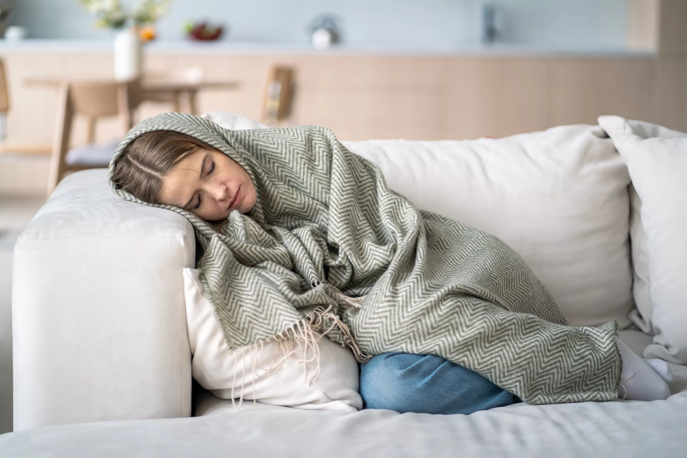 Exhausted, lost woman rests lifeless on couch wrapped in blanket,