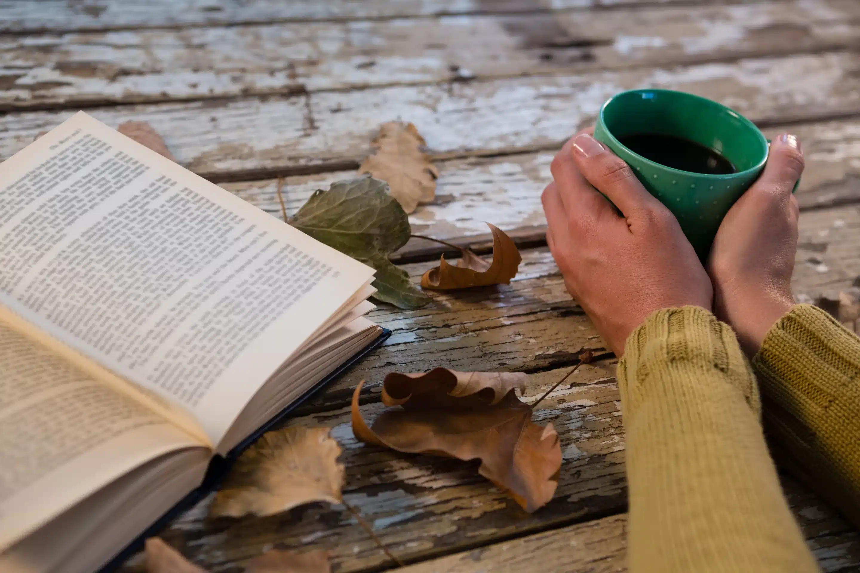 Cropped hand of woman holding coffee cup by book on wooden table