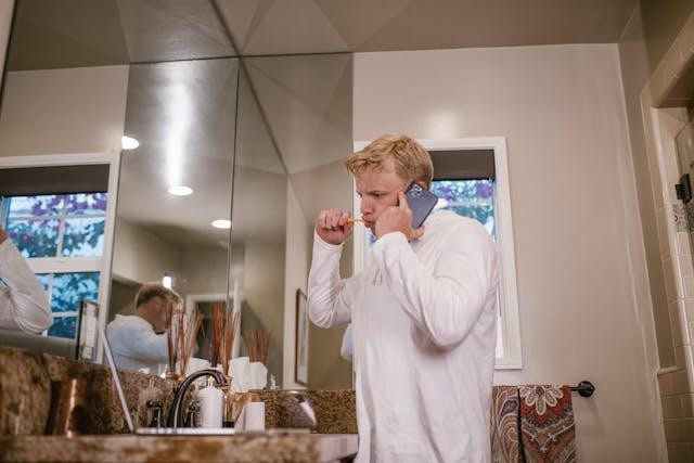 A man brushing his teeth while holding his phone