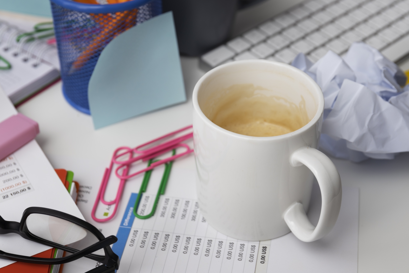 Messy office desk with scattered documents, coffee cup, and stationery