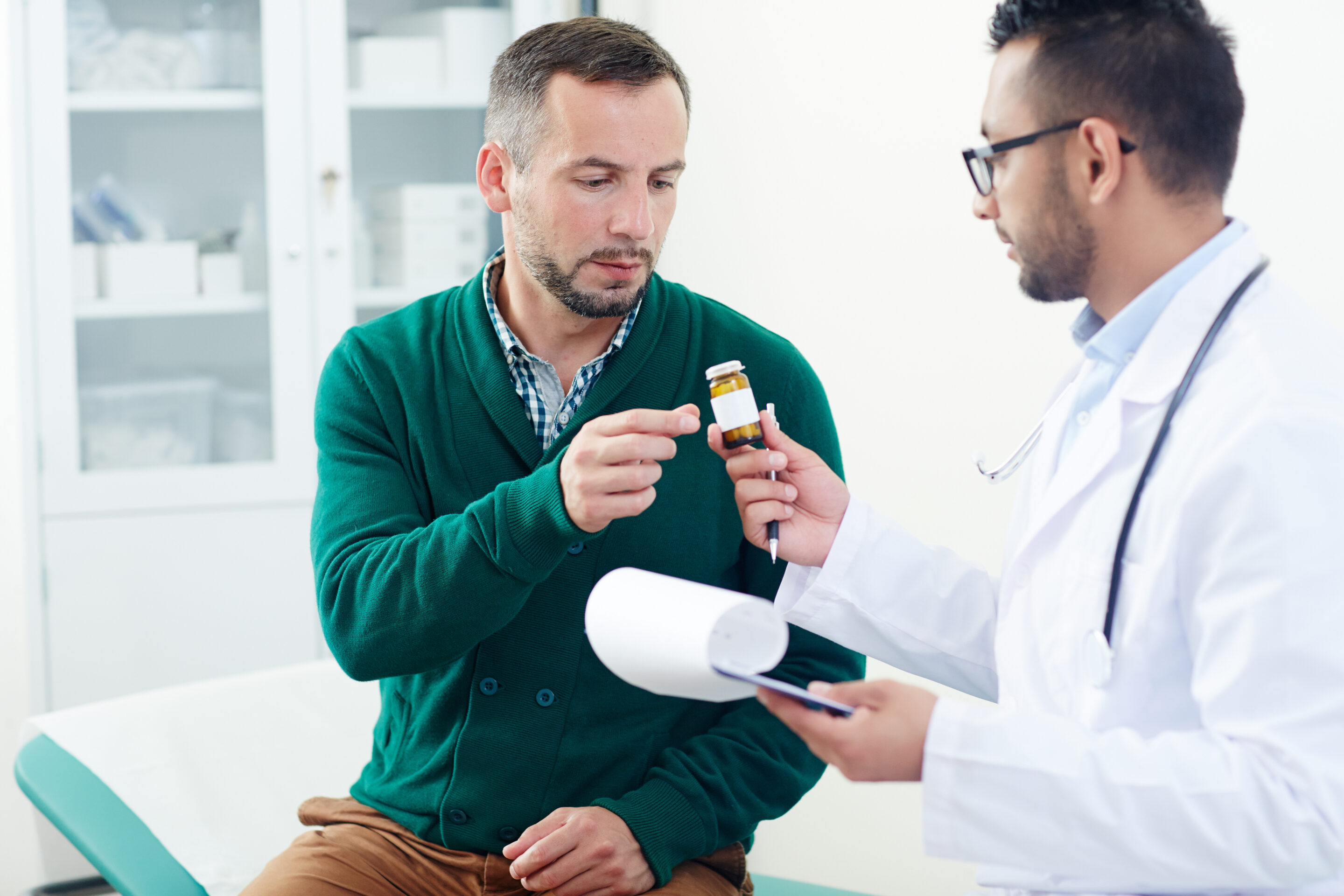 Doctor in white coat handing a bottle of pills to a patient wearing a green sweater
