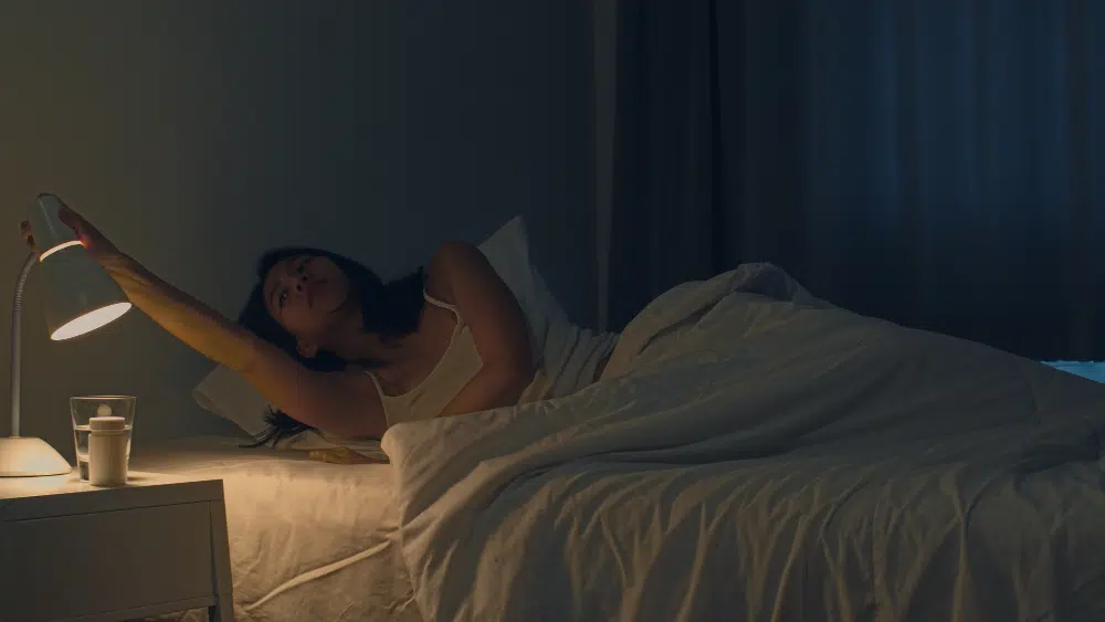 Woman turning off bedside lamp before going to sleep in cozy bedroom