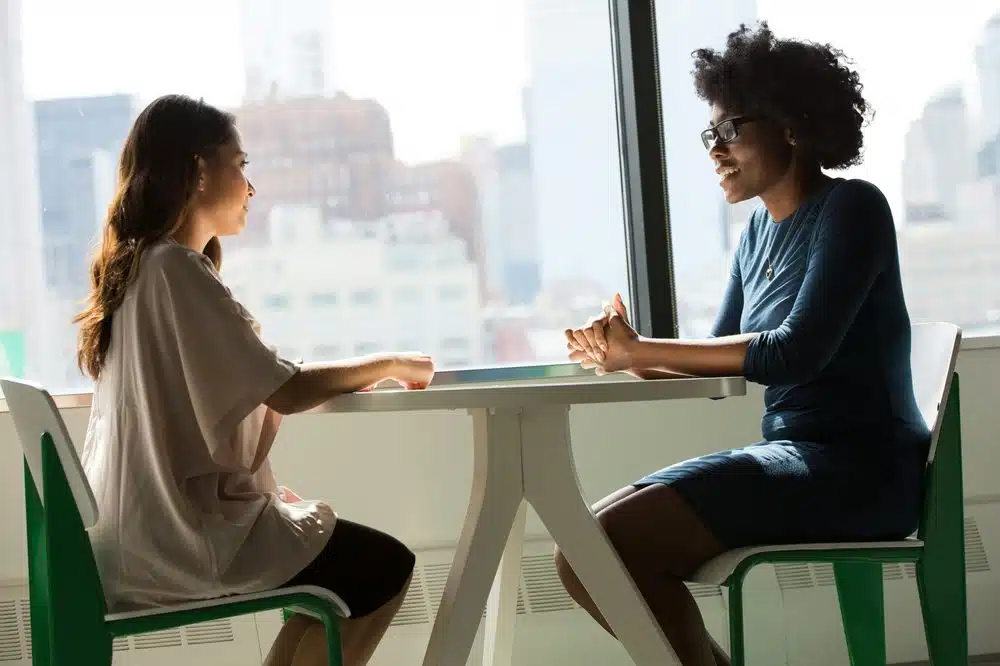 Two women having therapy conversation at table by window